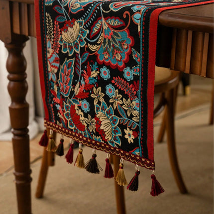Decorative table runner with intricate patterns and tassels on a wooden table.