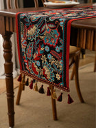 Decorative table runner with intricate patterns and tassels on a wooden table.